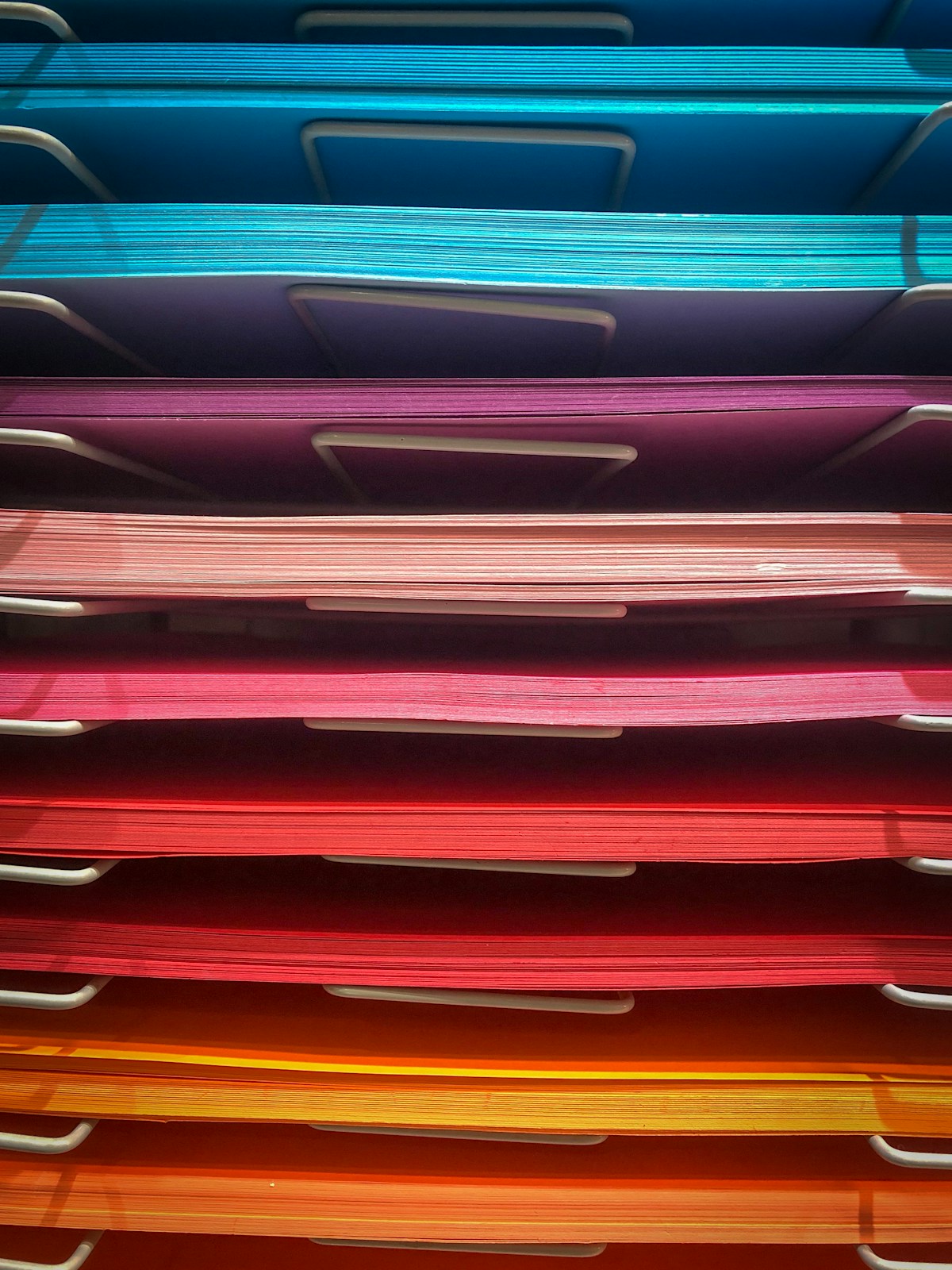 Stacked paper trays holding sheets of coloured paper, from blue at the top to orange at the bottom